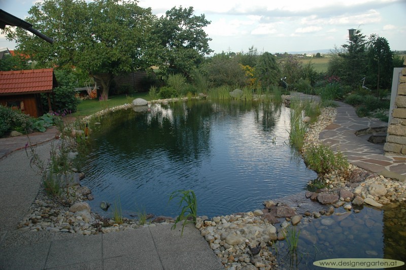 Swimming pond edged with river rock and a stone terrace, Austria
