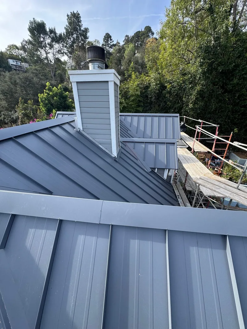 Finished charcoal standing-seam metal roof and chimney under a clear sky in the Hollywood Hills